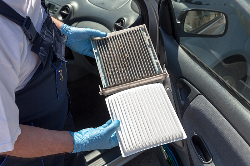 A mechanic holding a dirty car air filter next to a clean white replacement.